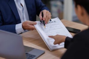 A couple reviews household documents at a kitchen table, taking photos of belongings for insurance records.