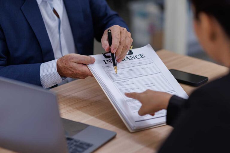A couple reviews household documents at a kitchen table, taking photos of belongings for insurance records.
