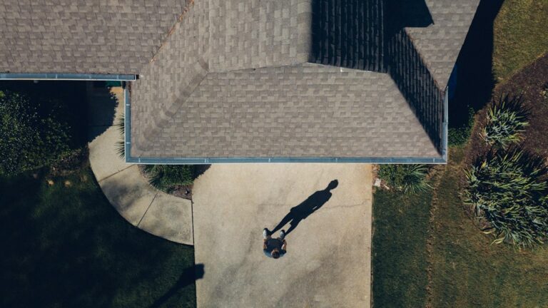 Homeowner photographs storm-damaged shingles while water drips into a bucket inside the house.